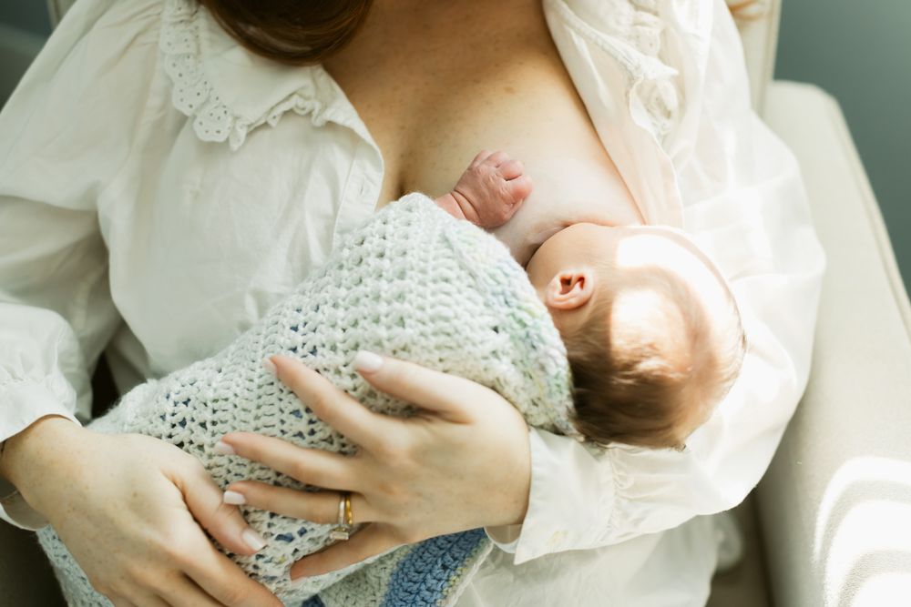 Mother wears a white peasant shirt breastfeeding newborn swaddled in a crochet blanket. Newburyport, Rye, Portsmouth newborn photographer