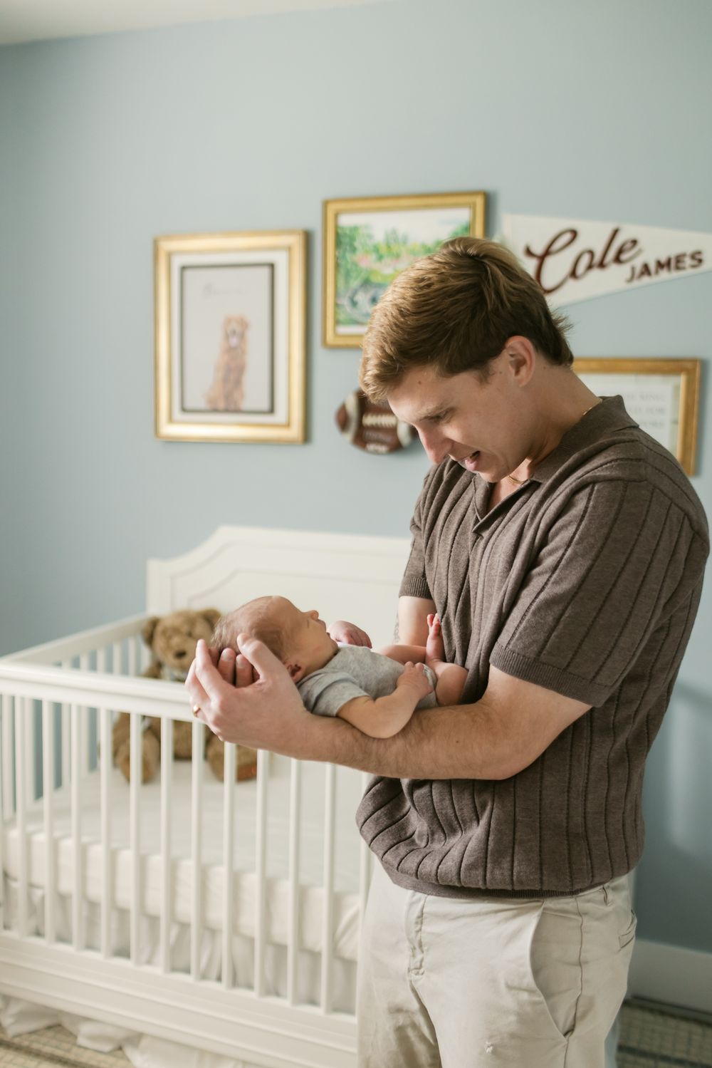 A blond father holds his newborn son in the baby nursery for newborn photos. Concord, Bedford, North Conway, Amherst newborn photographer.