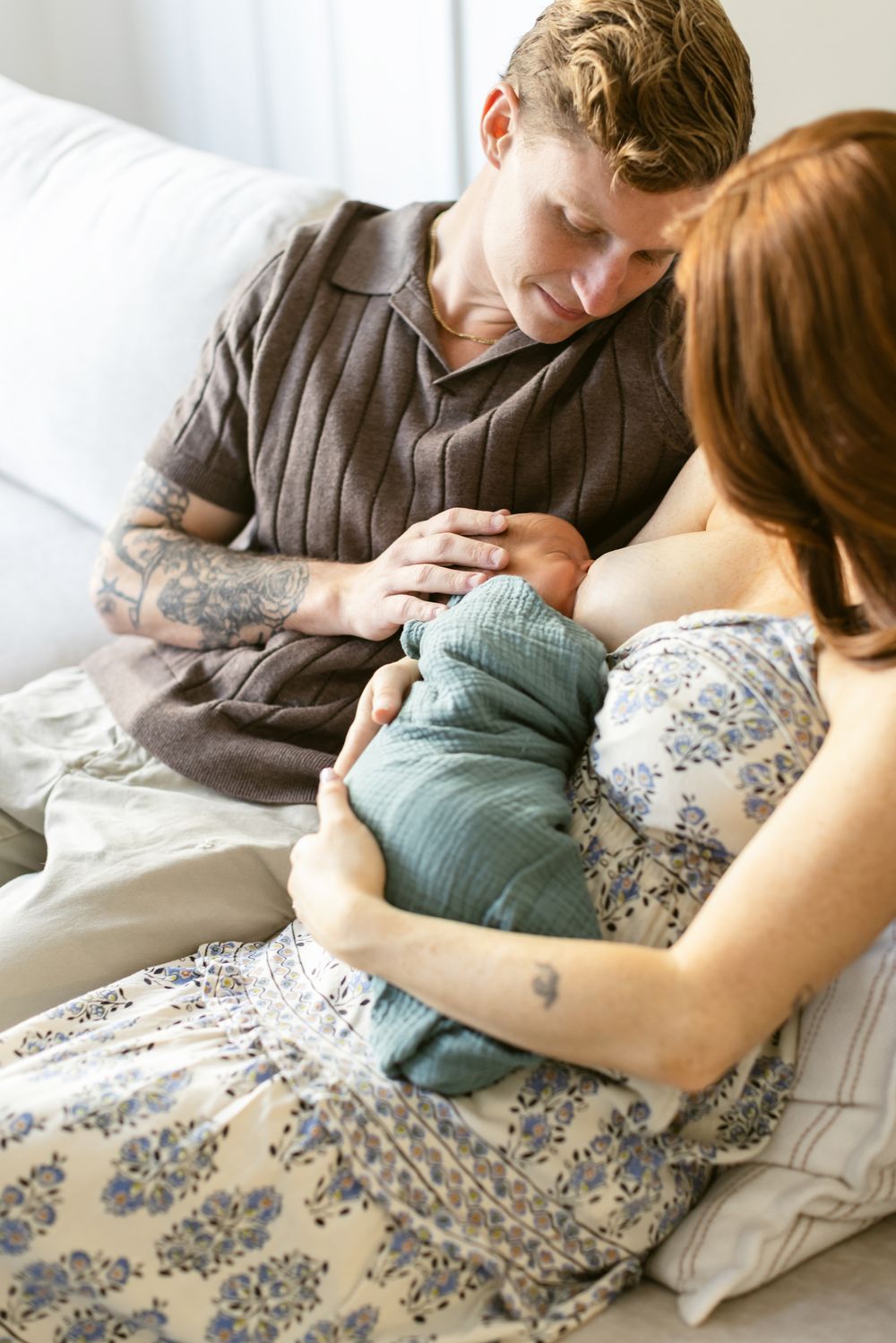 A red-haired mother breastfeeds her newborn son while father looks on touching baby's head. Lakes Region, Newburyport newborn photographer.