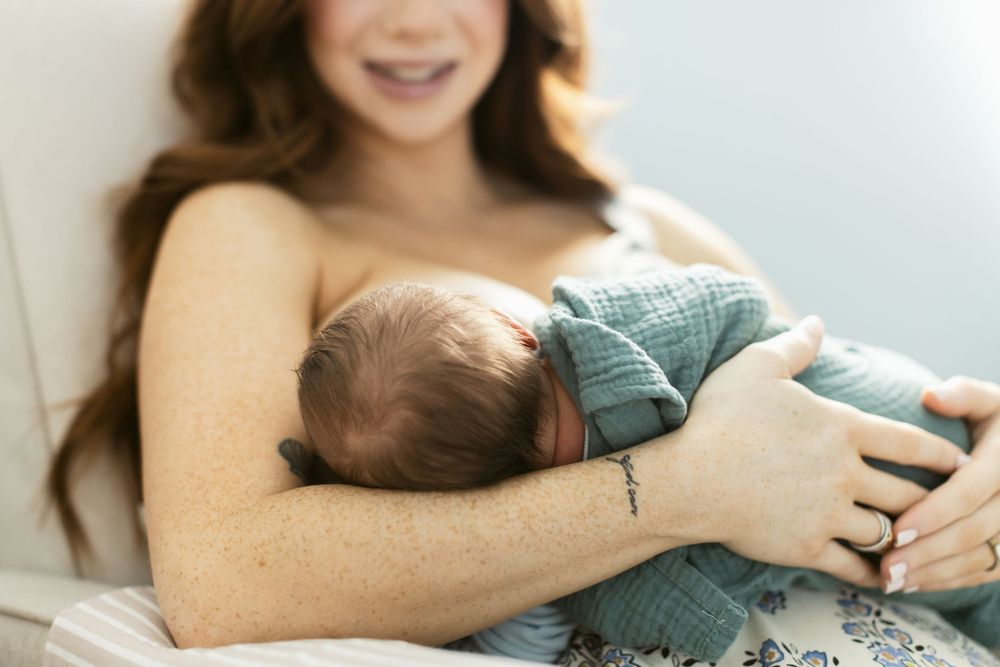 A red-haired mother with long hair smiles as she breast feeds her newborn son. Lenox, Central and Western MA newborn photographer.