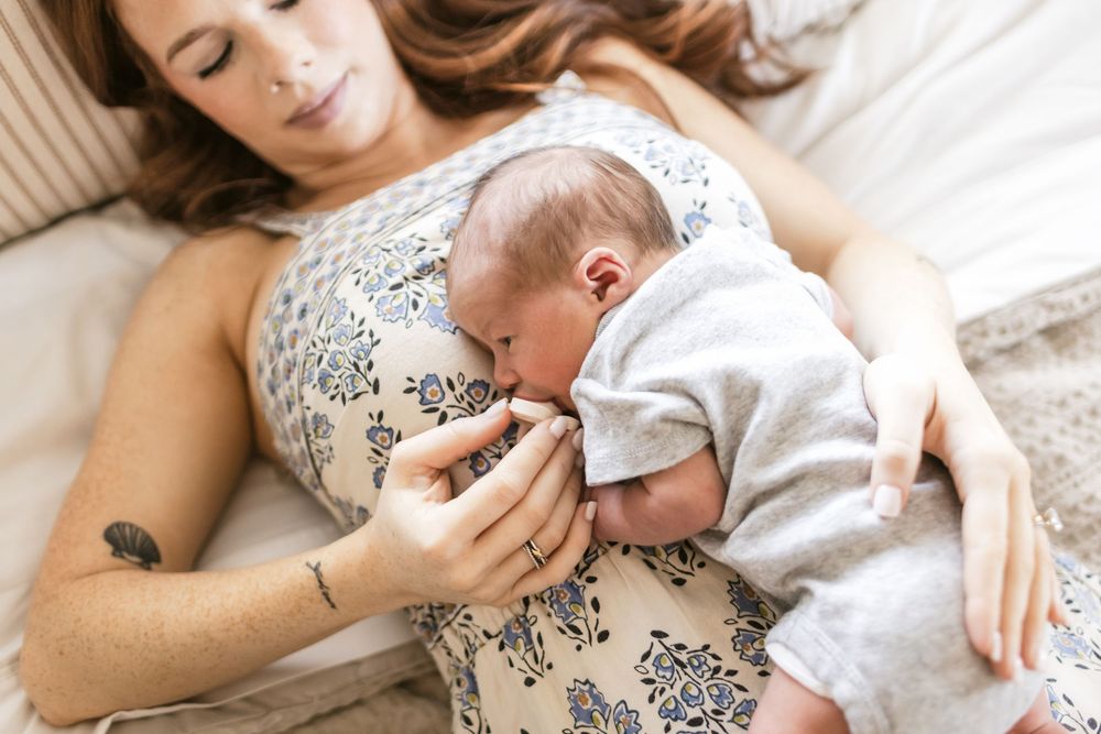 A red-haired mother lays on her bed with her newborn son resting on her chest. Essex, Gloucester North Shore newborn photographer.