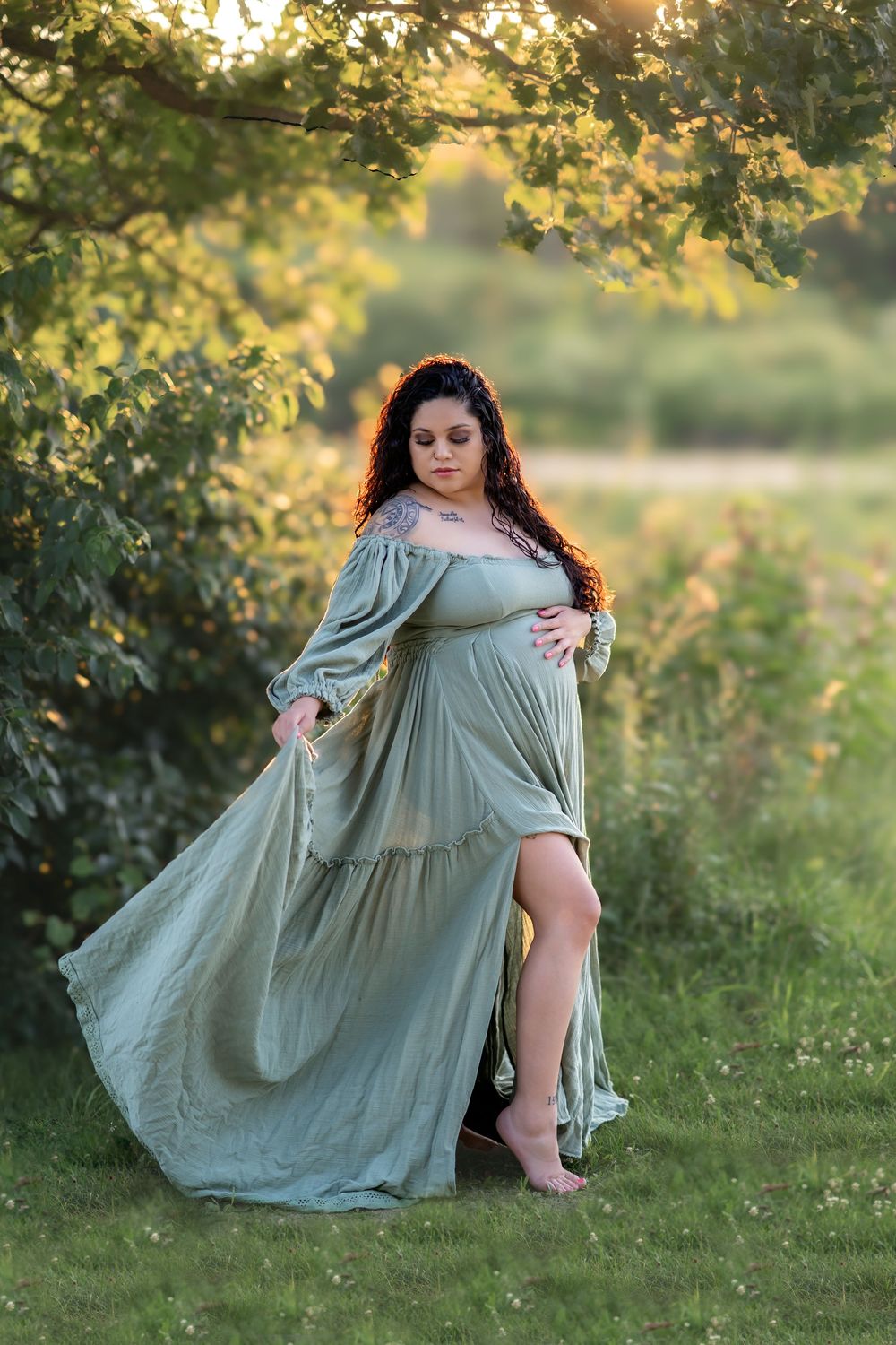 Flowing sage green dress catches golden sunlight in dreamy outdoor portrait among summer foliage.