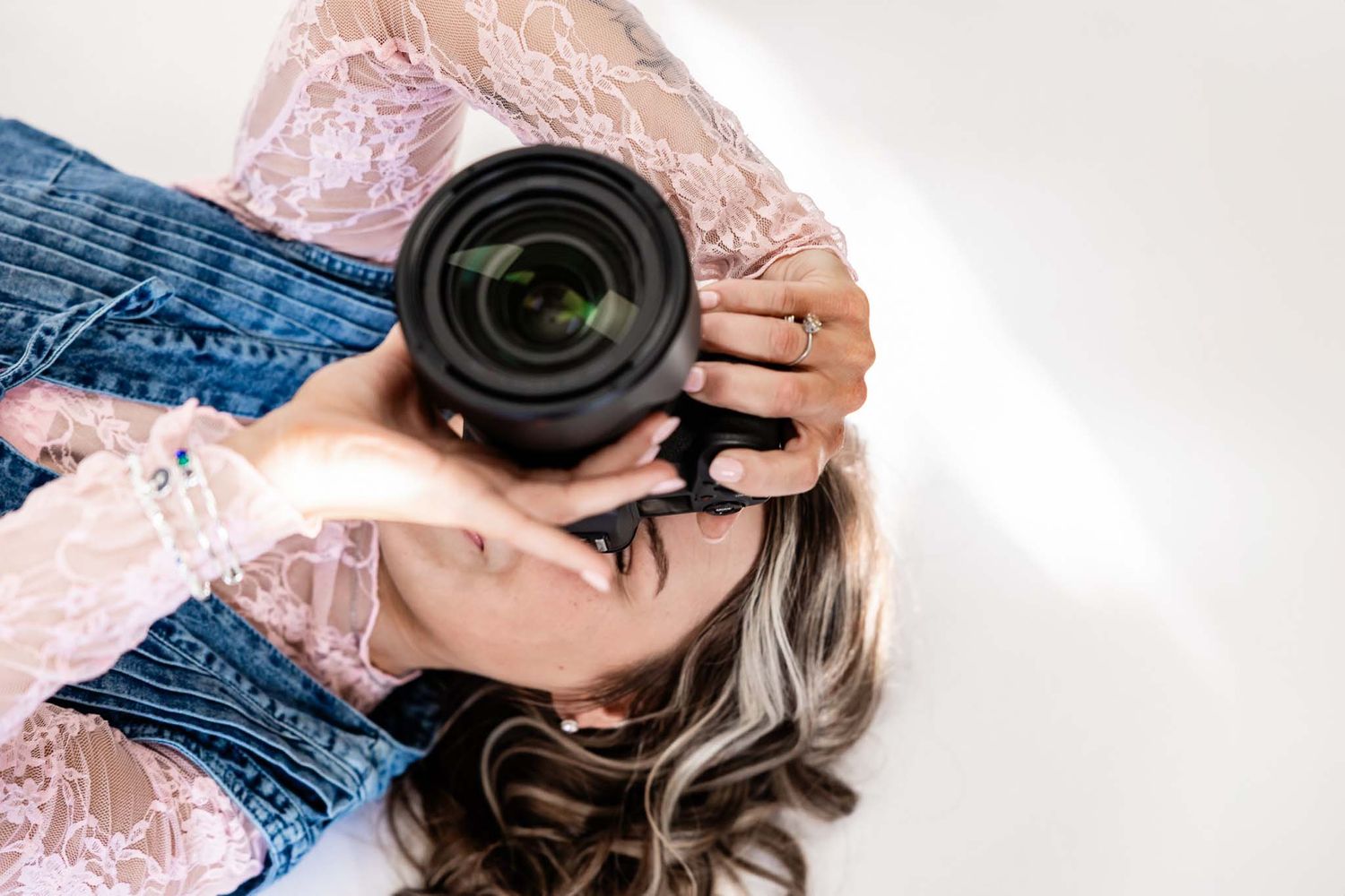 Wyoming Photographer
Hands holding a professional camera with lens while wearing lace top and denim against white background.