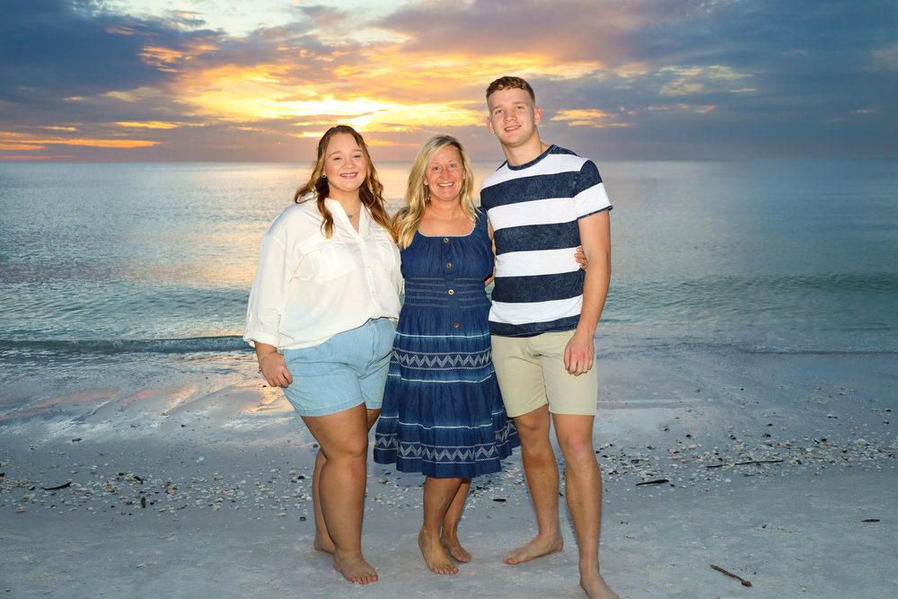 A mother and her children posing along a beach at sunset with vibrant orange and blue sky colors.
