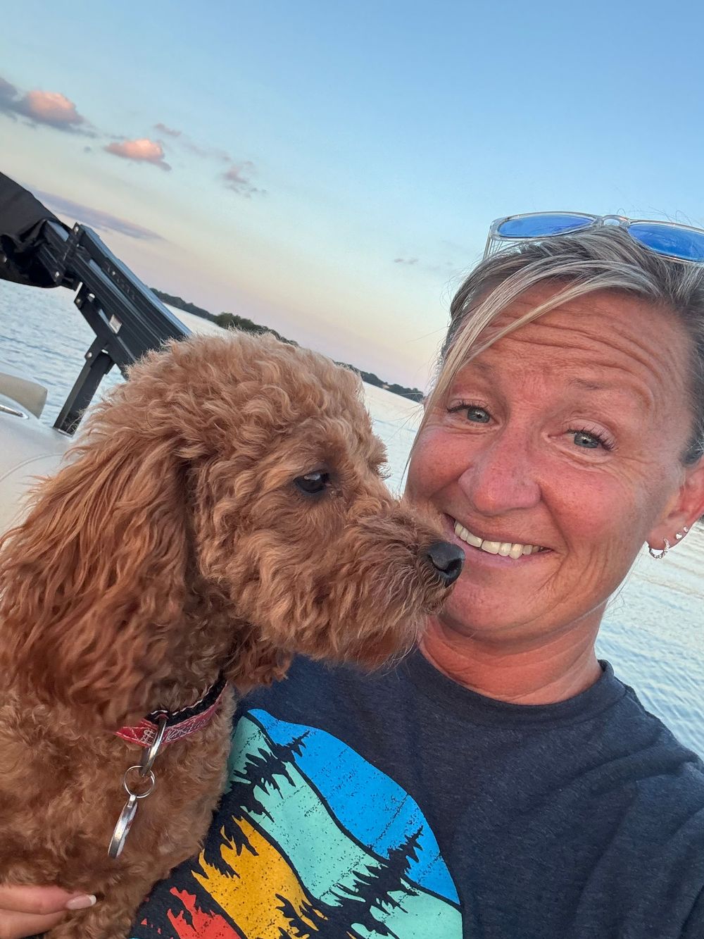 A selfie of a photographer showing her holding a  fluffy mini labradoodle dog against a beach sunset backdrop.
