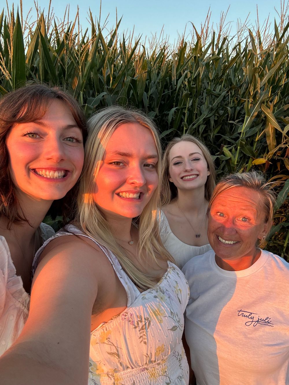 A group poses in front of a cornfield at sunset with warm orange lighting casting a glow on their faces.  Photo taken in Lawton, Iowa.