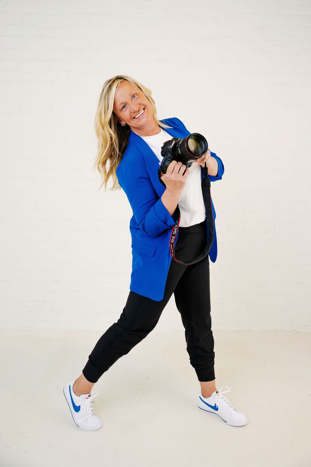 Photographer in bright blue blazer and black pants poses playfully against white background.