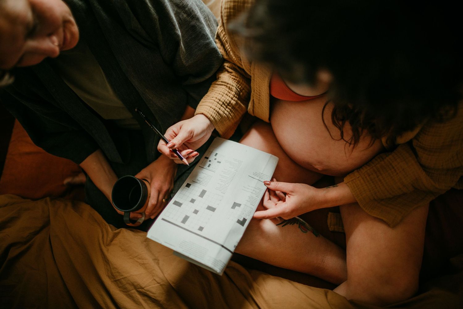 queer couple does a crossword puzzle in bed in-home documentary photography session portland oregon rushes & waves