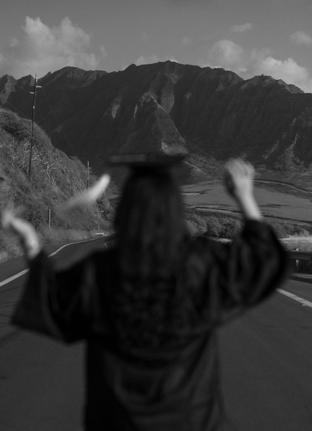 A silhouetted figure raises their arms while standing on a scenic mountain overlook against dramatic mountain peaks.