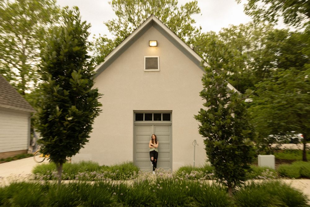 Small white church-style building with a blue door flanked by two tall evergreen trees in a residential setting.