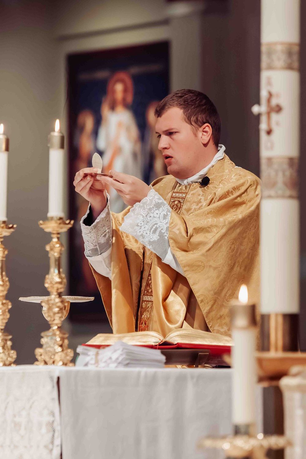 Catholic priest in golden vestments elevating the Eucharist during Mass at a candlelit altar.