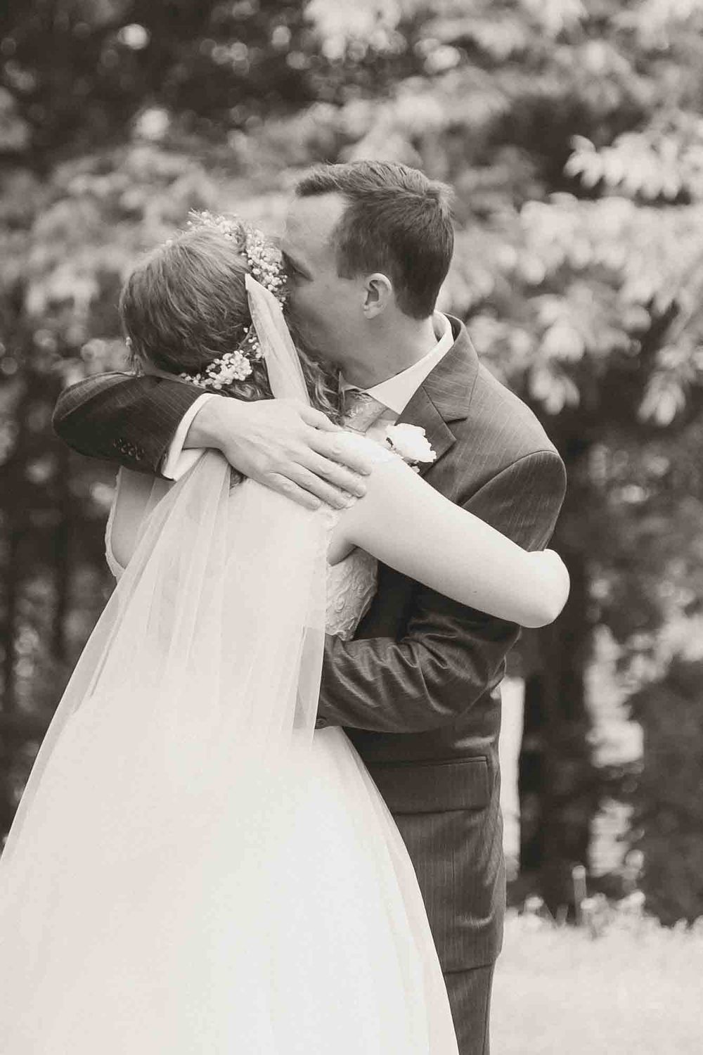 Black and white photo of a bride and groom sharing a romantic kiss outdoors on their wedding day.