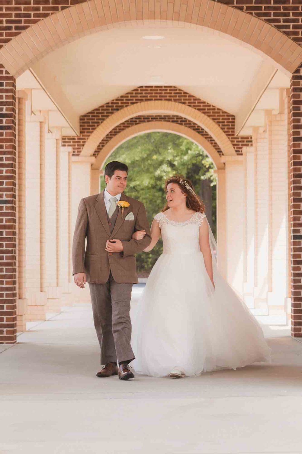 Bride and groom walking hand in hand under elegant brick arches in wedding attire.