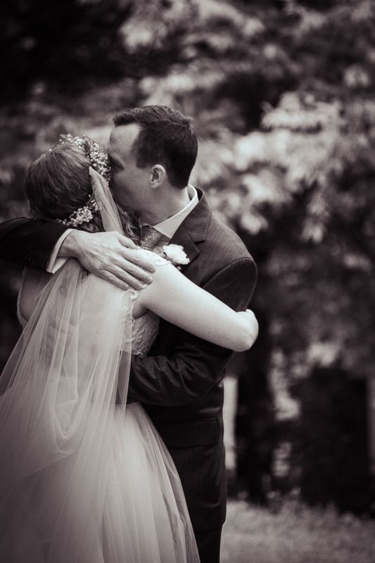 Black and white photo of a bride and groom sharing a kiss outdoors, with the bride in a veil and groom in a suit.