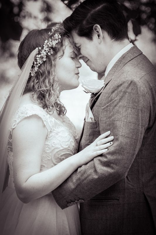 Black and white photo of a bride and groom sharing a romantic moment, bride wearing floral crown and veil.