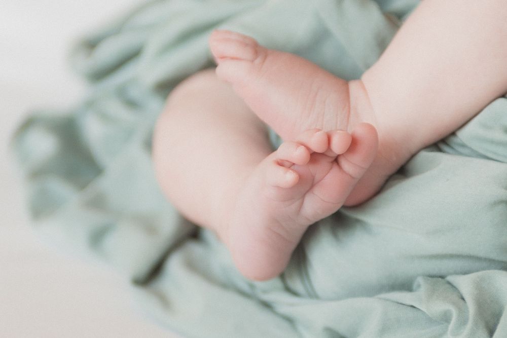 Close-up of tiny newborn baby feet resting on a soft sage green blanket.