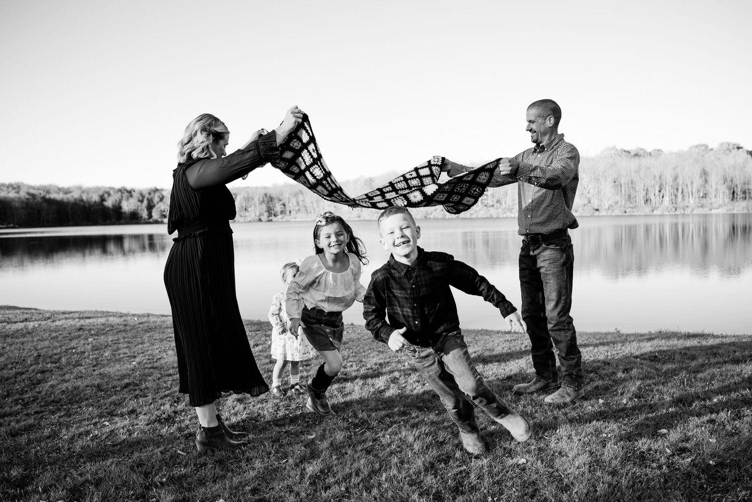 Series of playful family moments captured in black and white on a grassy hillside.