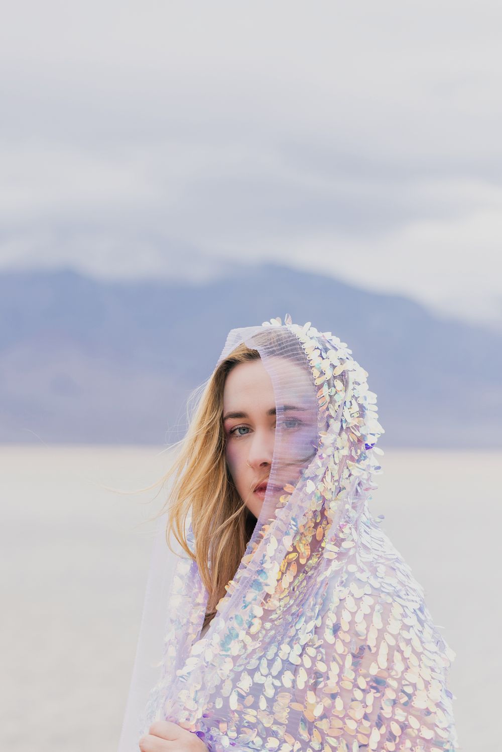 Ethereal portrait with iridescent holographic material creating a dreamy effect against a misty mountain backdrop.