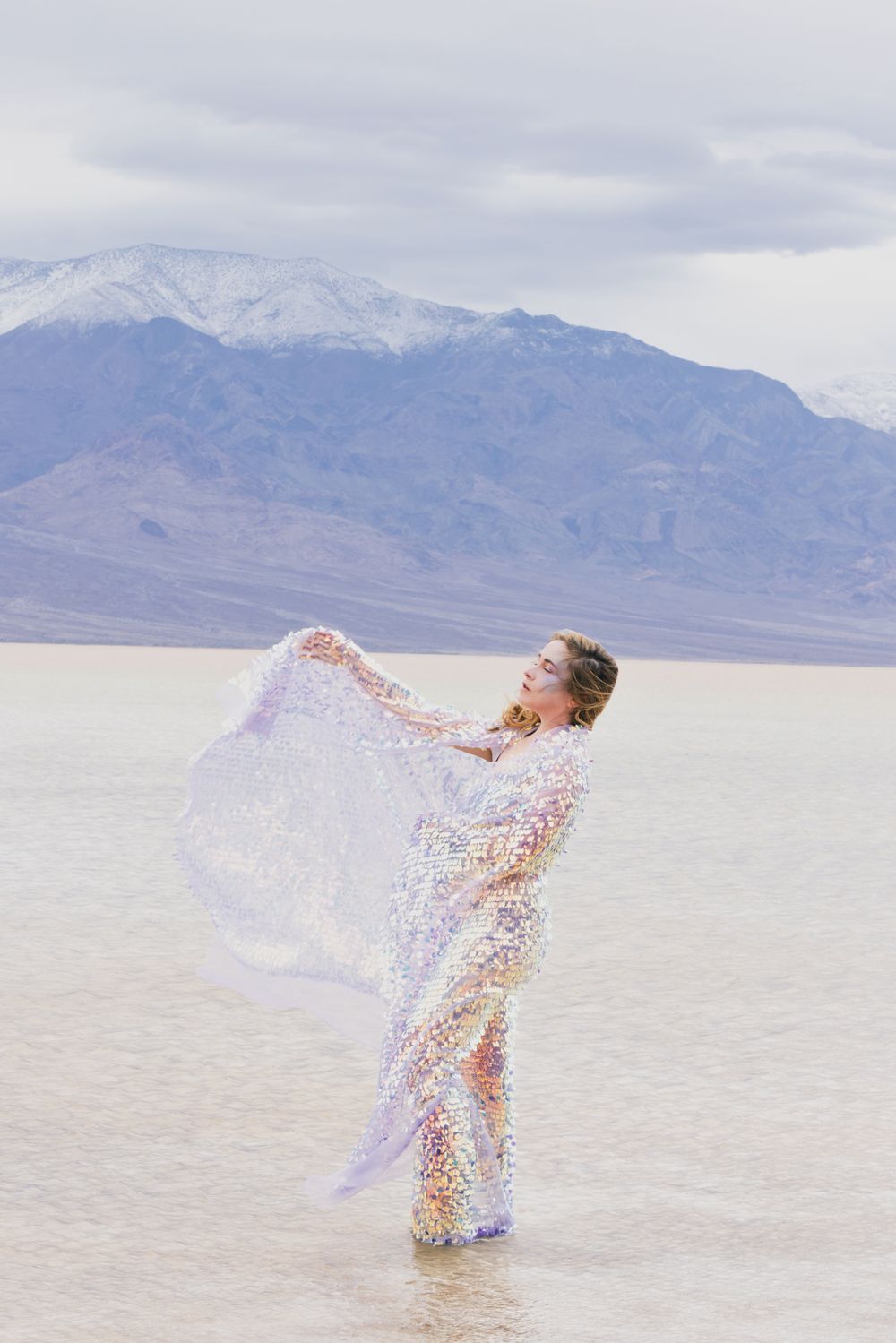 Ethereal figure in flowing white dress dancing on salt flats with mountains in background.