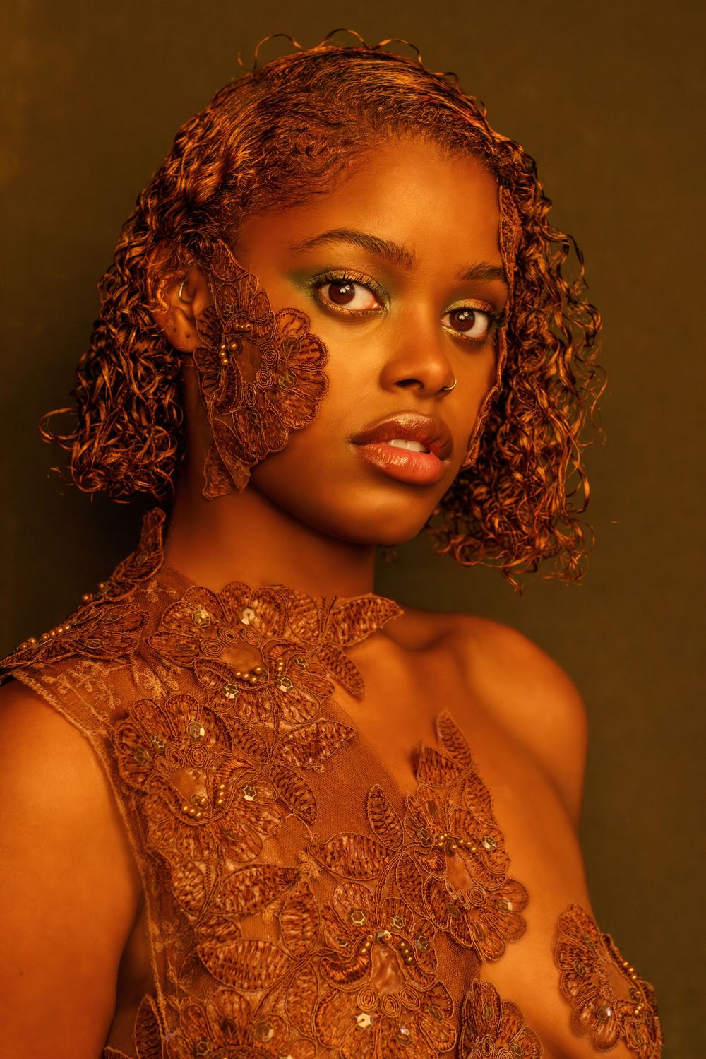 Glamorous portrait featuring intricate golden body art and jewelry against a warm brown background.