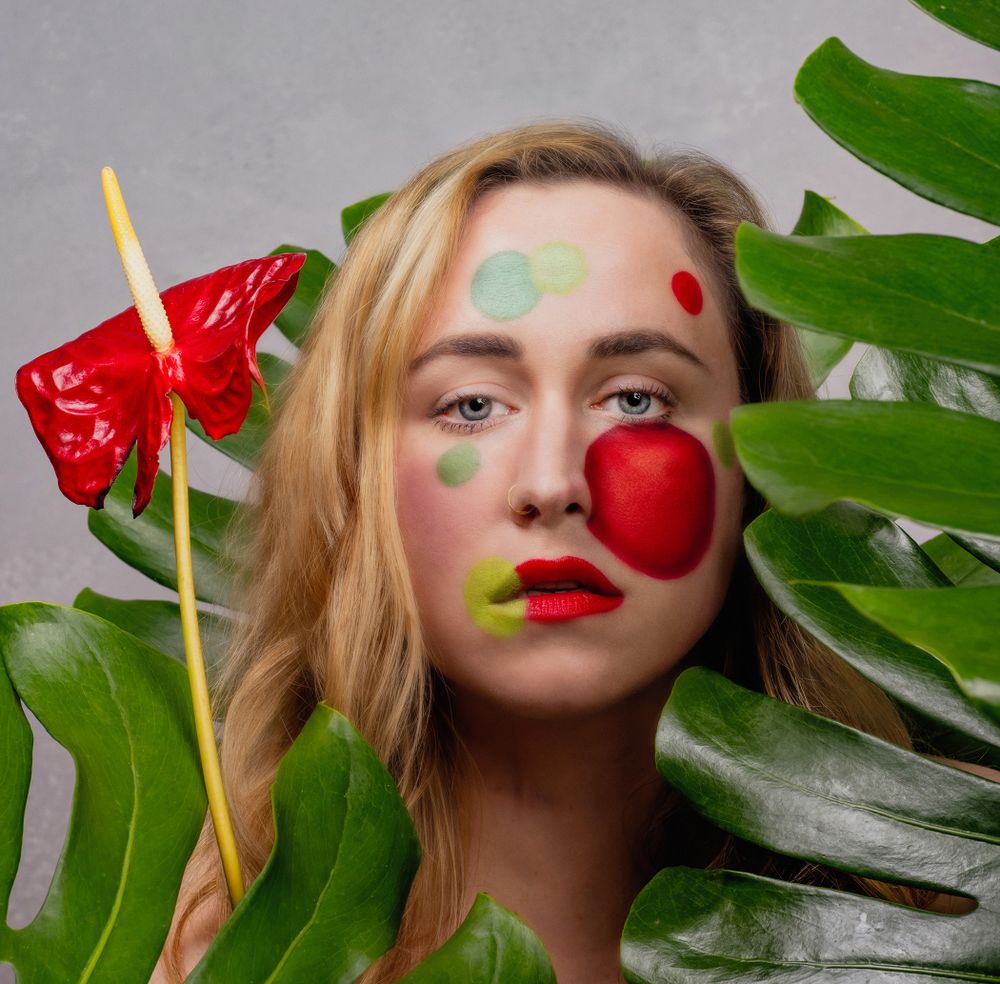 Creative beauty portrait with tropical leaves and vibrant red lip art details.