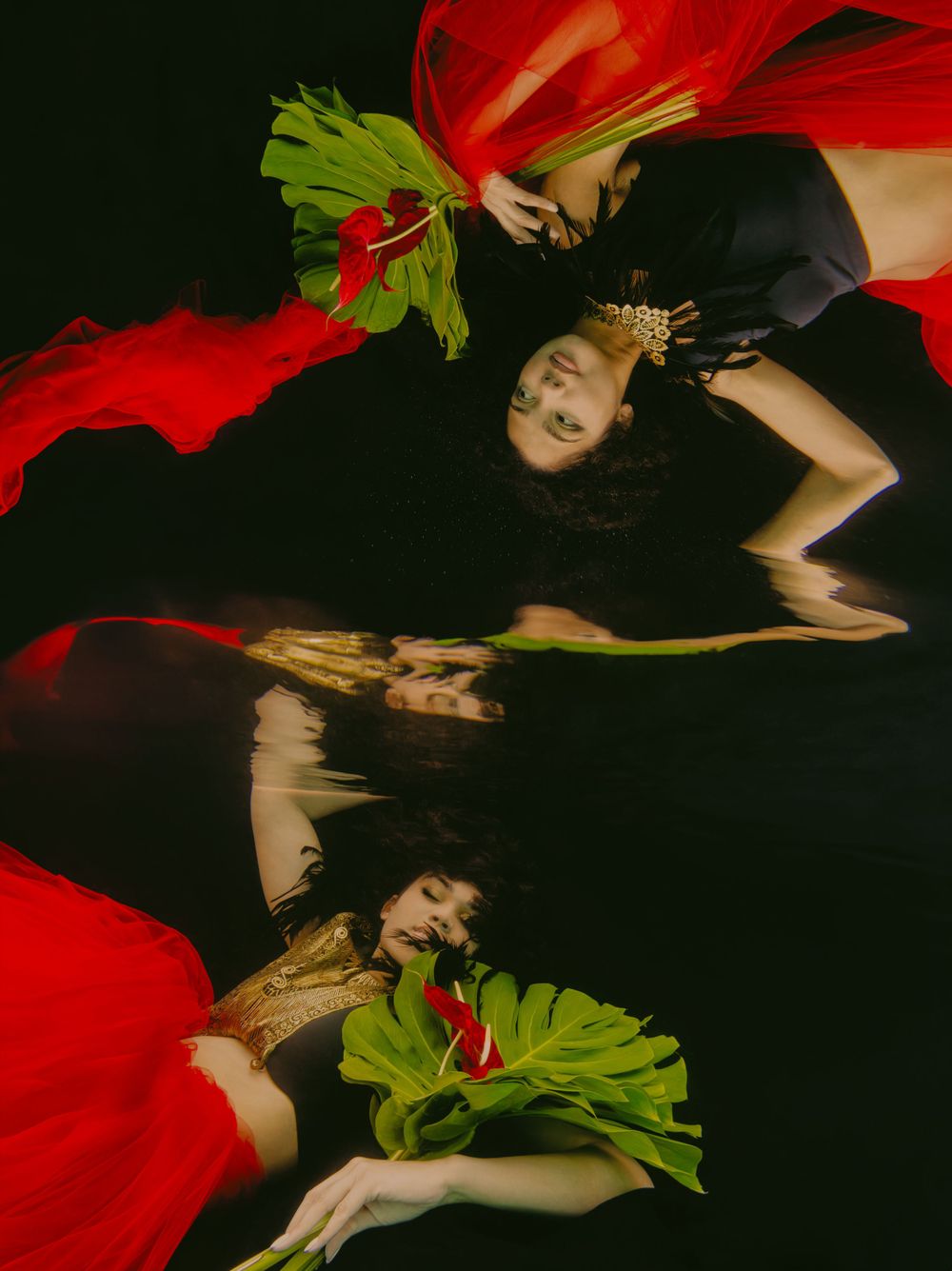 Dramatic fashion scene with red fabric and green leaves in dark setting.