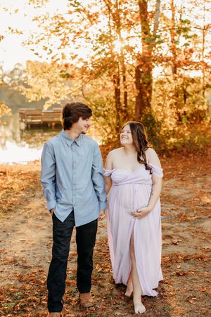 A couple walking together during a fall maternity photoshoot near a lake.