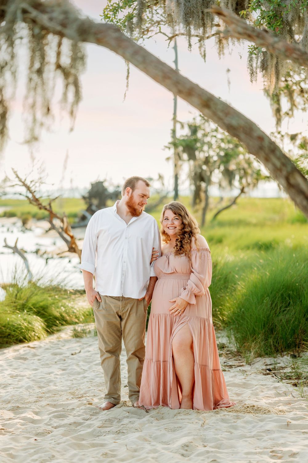 Expecting couple in pink dress and white shirt pose together at Goose Creek State Park.