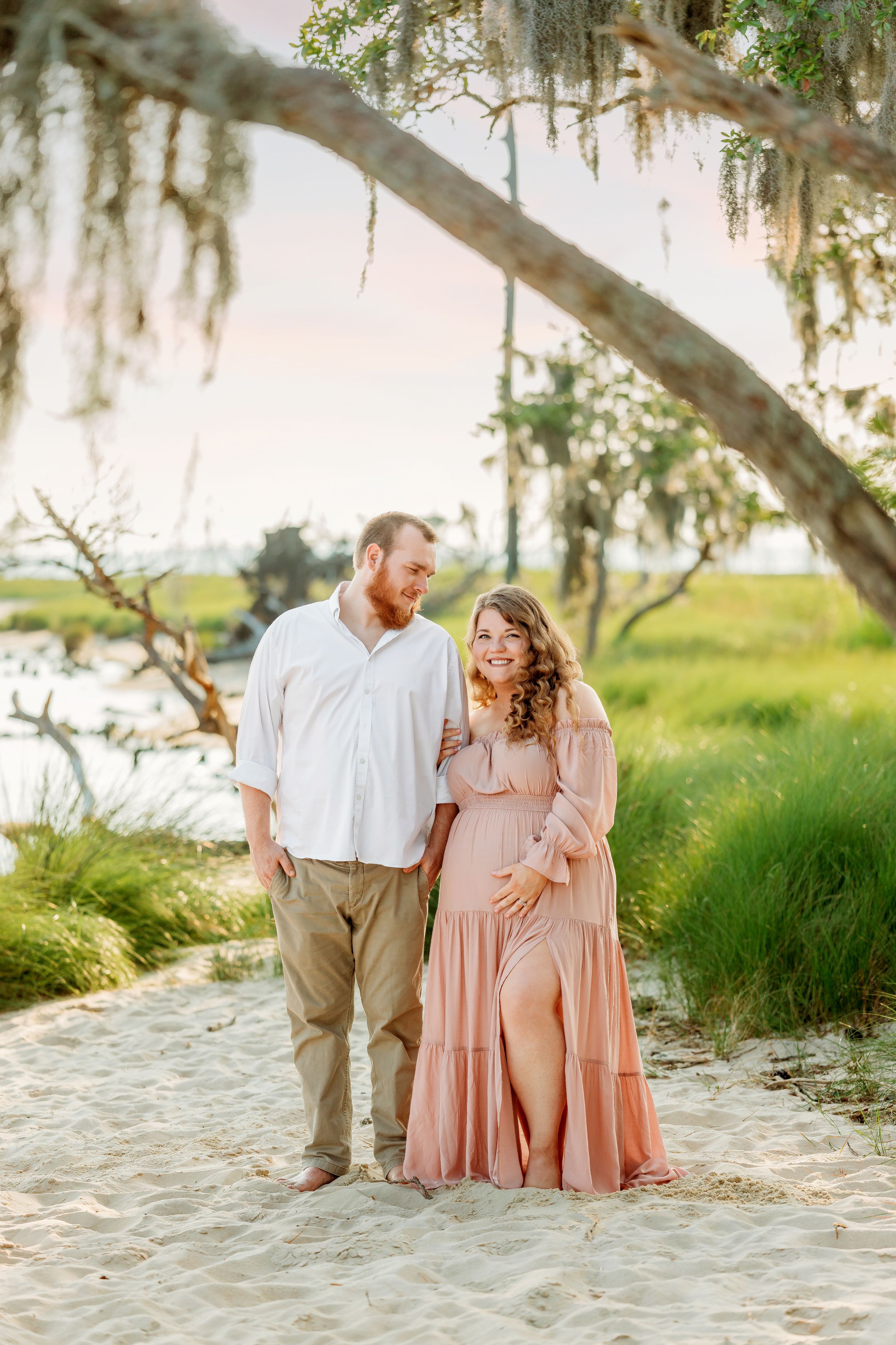 Expecting couple in pink dress and white shirt pose together at Goose Creek State Park.