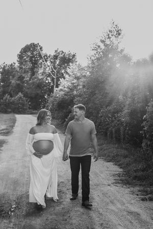 Couple walking together on a sunlit rural path during maternity photoshoot.