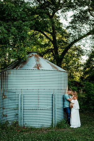 Maternity photoshoot by rustic metal grain silo in natural outdoor setting.
