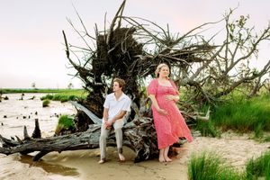 Sunset maternity photos among driftwood on coastal beach.