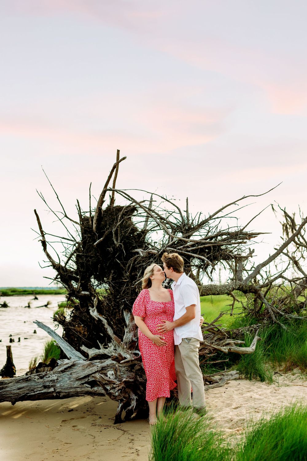 Couple's maternity session at sunset with driftwood and coastal scenery.