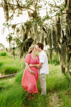 A couple in a red polka dot dress and white shirt share romantic moments among Spanish moss-draped trees.
