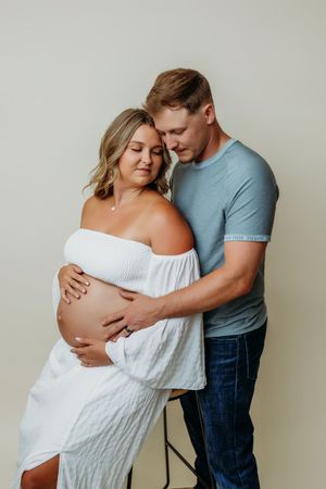 Maternity photo series showing couple in tender embrace against white background.