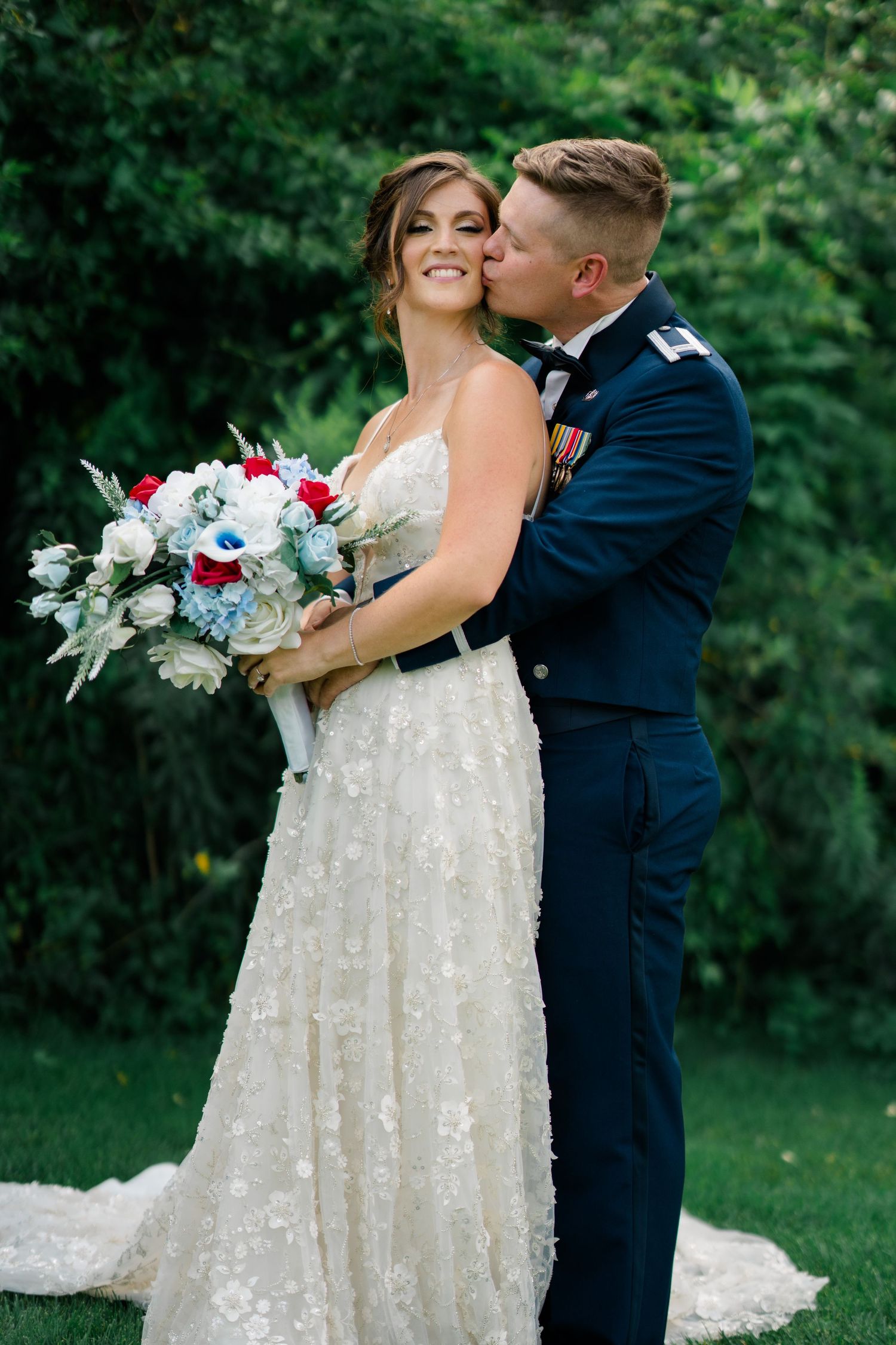 A couple in wedding attire embraces while holding a bouquet of blue and white flowers.