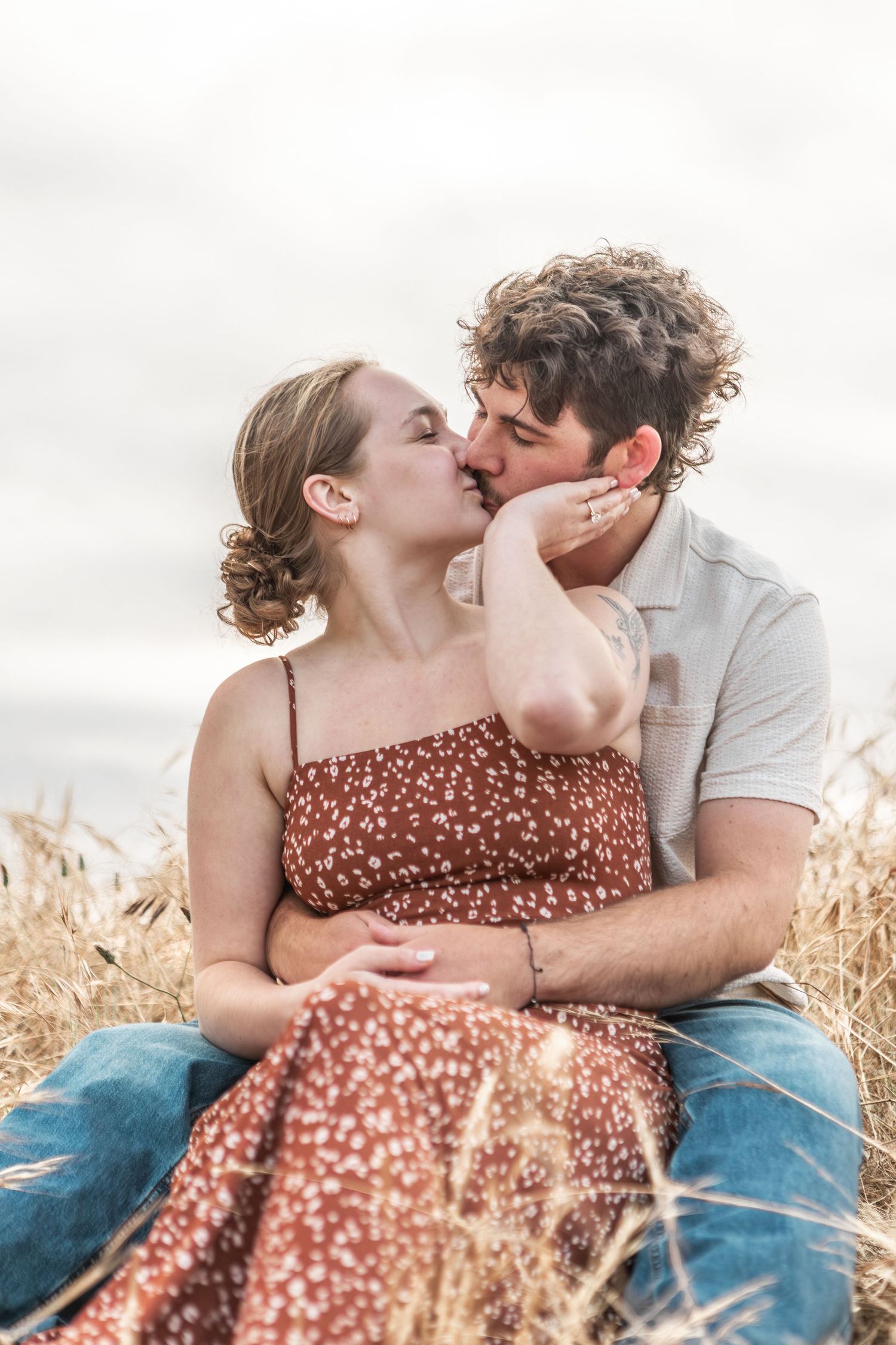 Candid engagement portrait of a couple kissing in a sunlit golden field