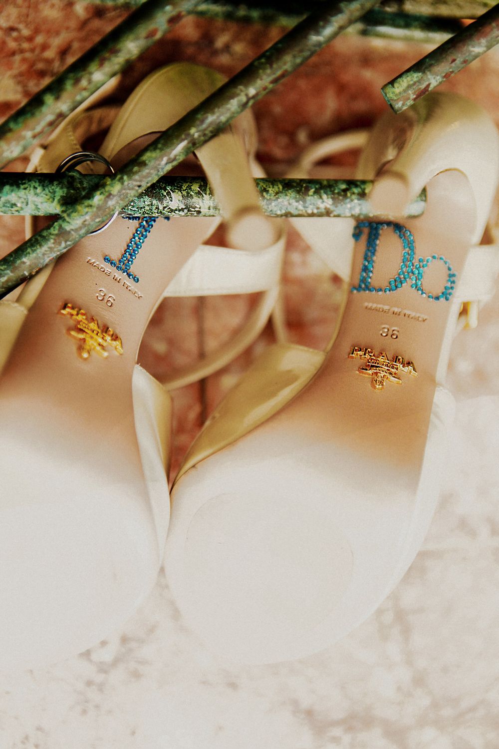 A pair of elegant white bridal shoes with blue lettering and gold butterfly decorations photographed against a textured backdrop.
