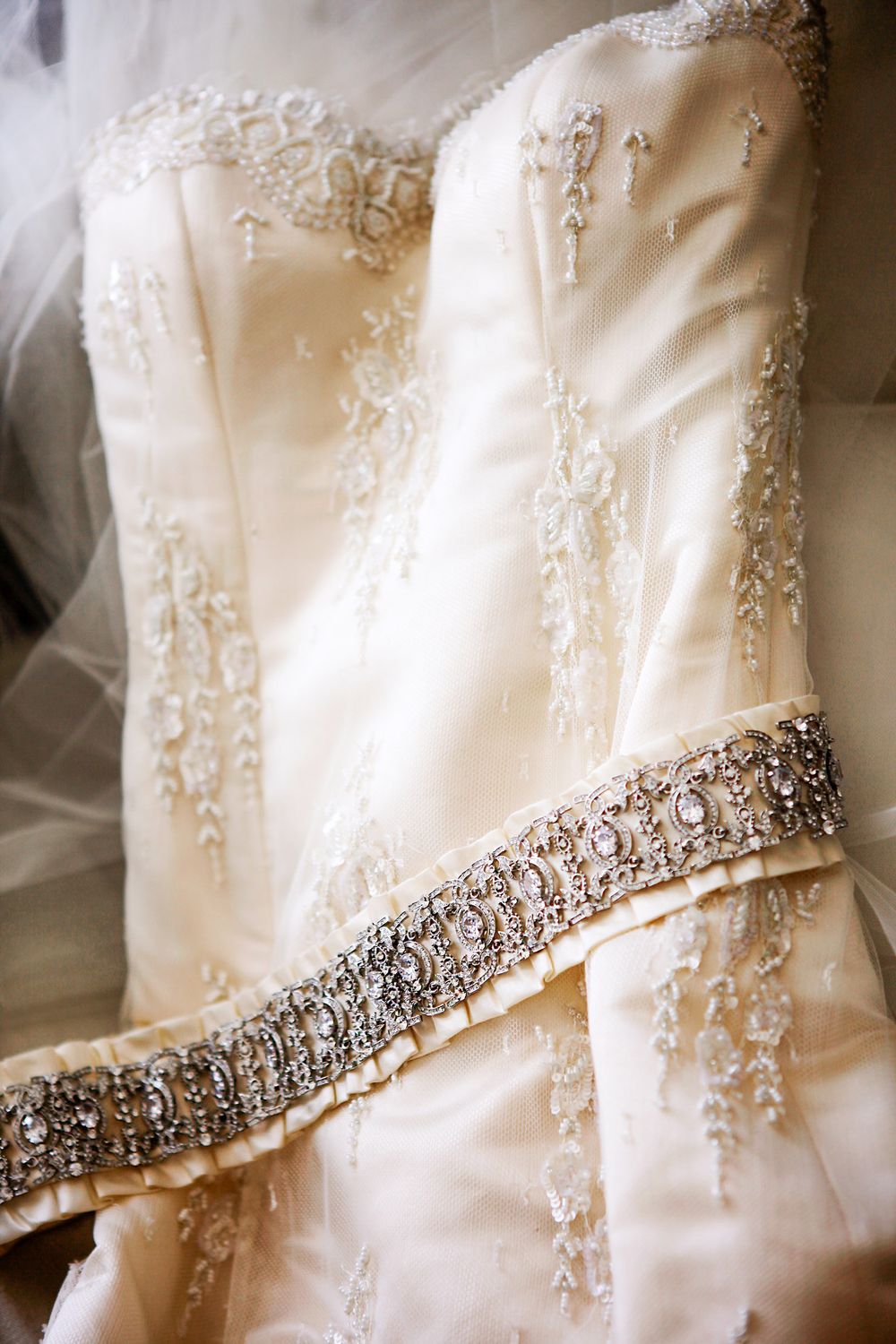 Close-up details of a wedding dress showing intricate beaded embellishments and crystal trim on ivory satin fabric.