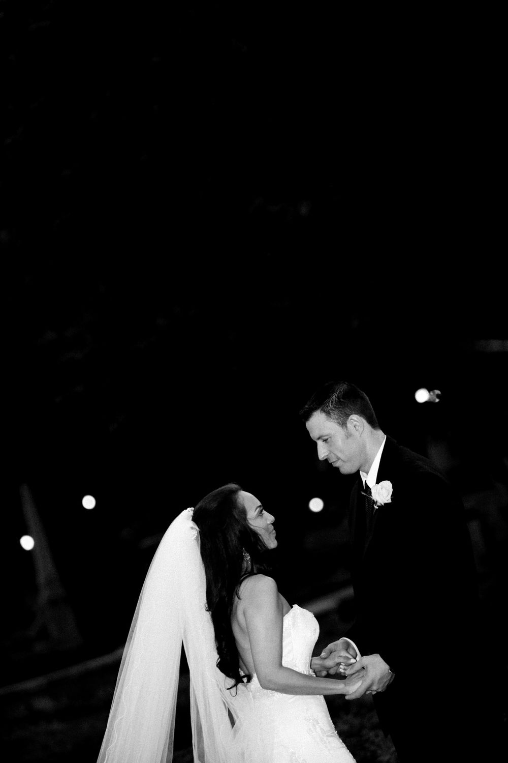 A black and white wedding photo of a couple dancing together, with the bride wearing a flowing veil and white dress.