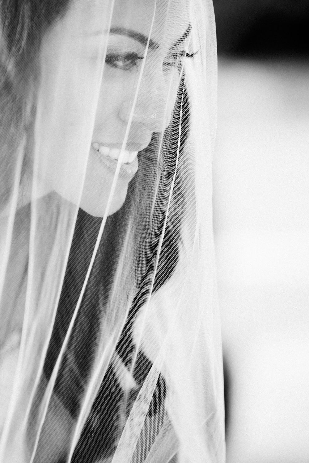 A black and white artistic portrait shows a person smiling through sheer white fabric for a dreamy ethereal effect.