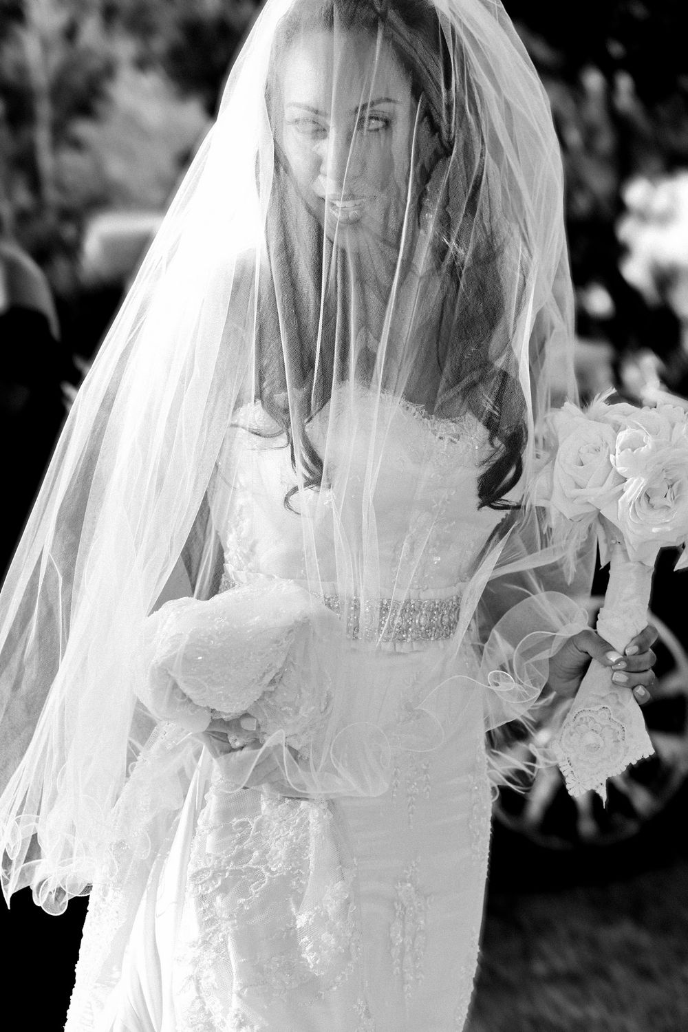 Black and white photos show a bride in a delicate lace veil and wedding dress moving gracefully through a garden setting.