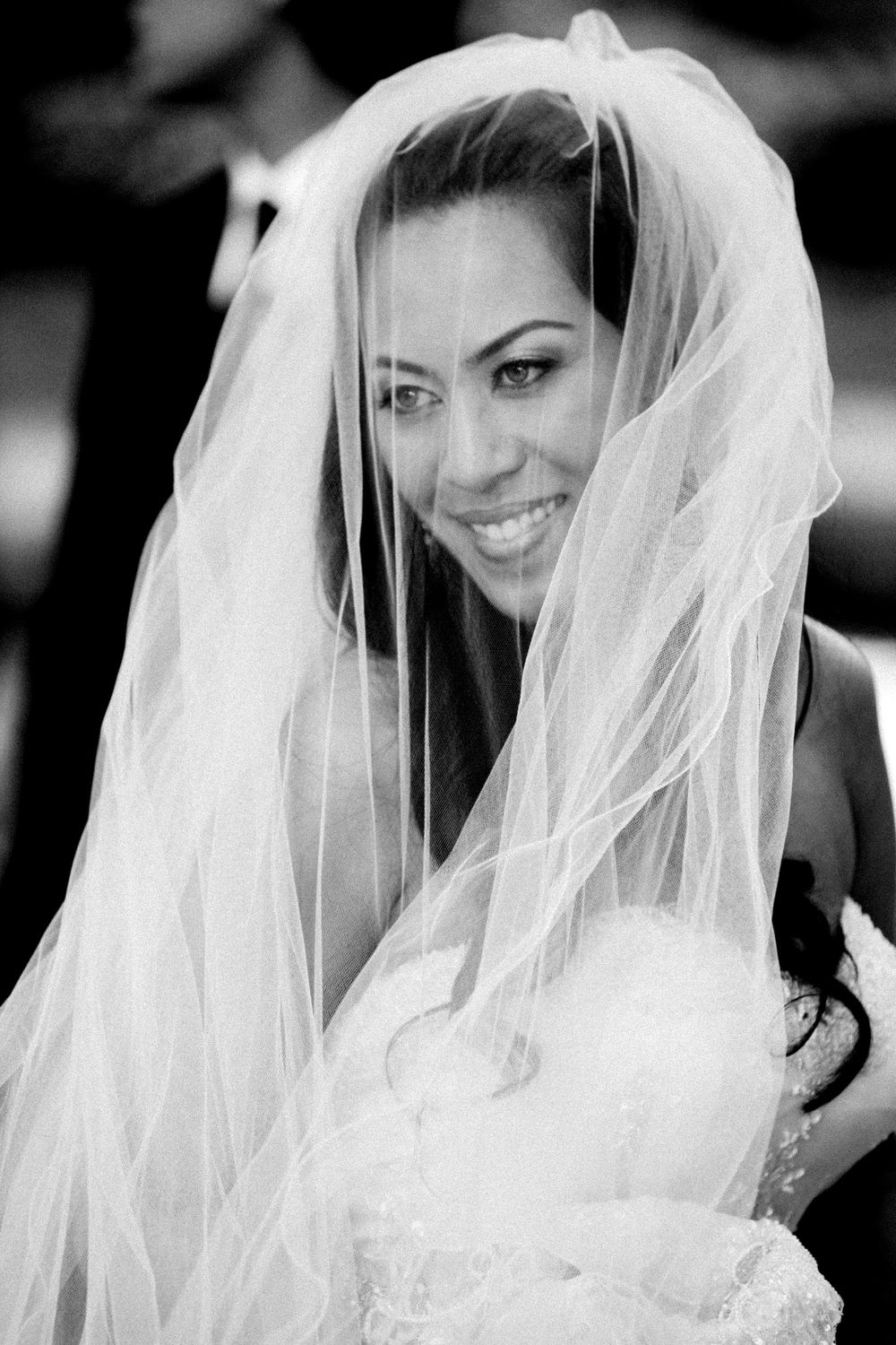 Black and white portrait of a smiling bride wearing a flowing white veil and wedding dress.