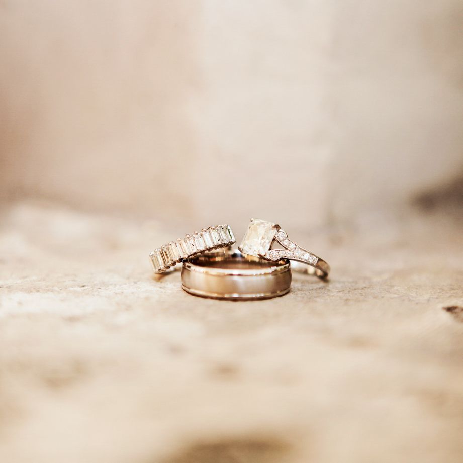 Wedding rings with diamonds arranged artistically on a textured beige surface in soft light.