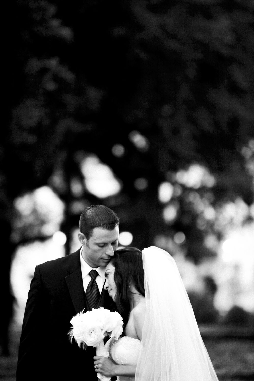 A black and white wedding photo showing a couple standing close together with the bride holding a white bouquet.