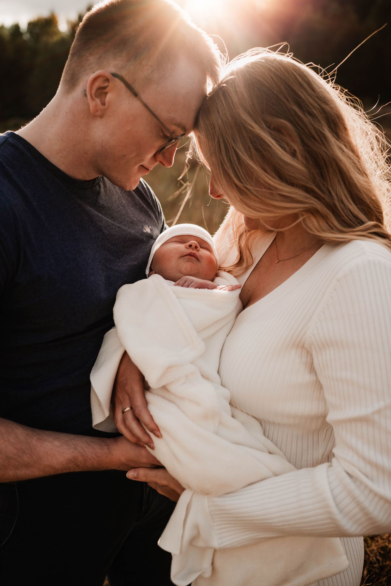 Mamma och pappa med sin nyfödda bebis ute på en äng i solendgången