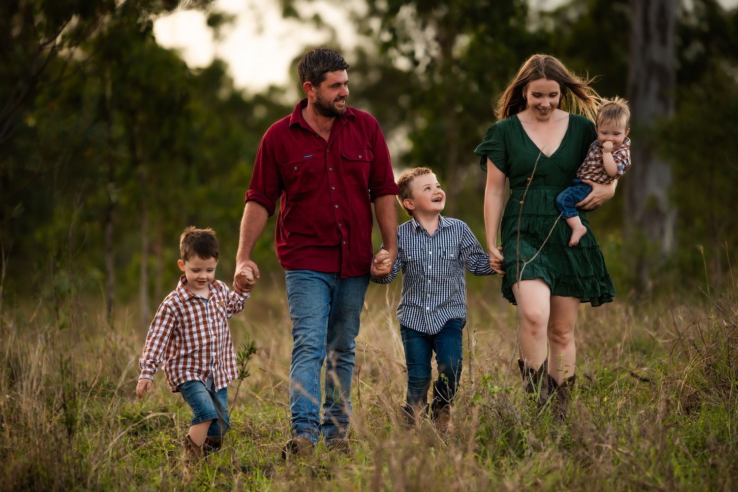 A family of four walking together through a sunlit field in casual clothing.