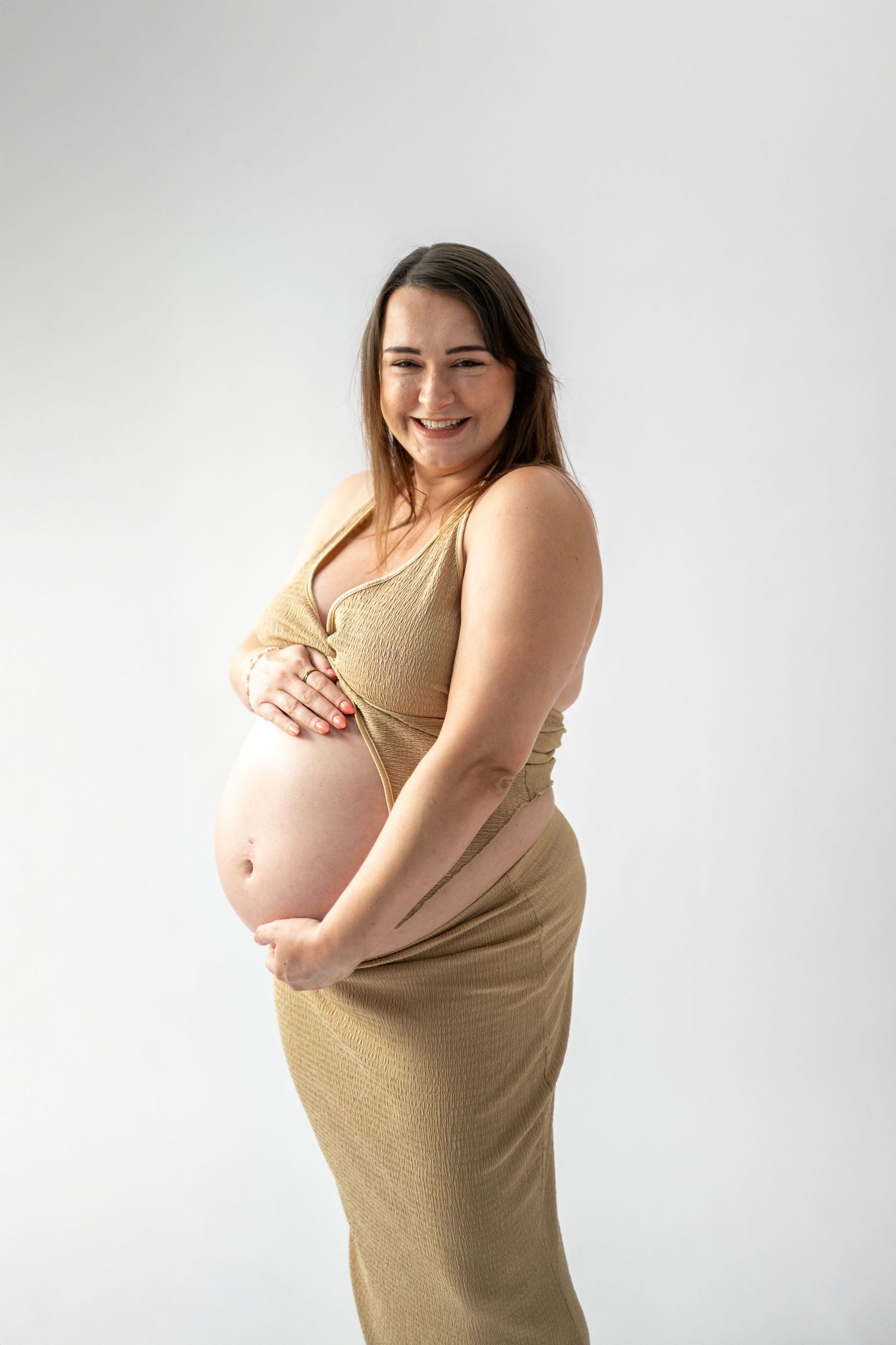 Maternity photos showing pregnant woman in beige dress against white background.