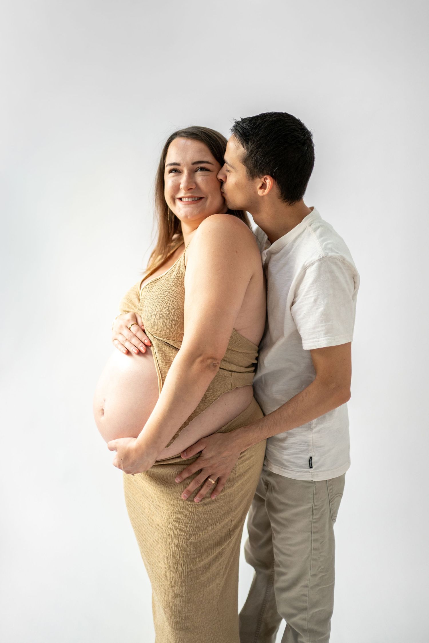 Intimate maternity photos of couple embracing against white backdrop.