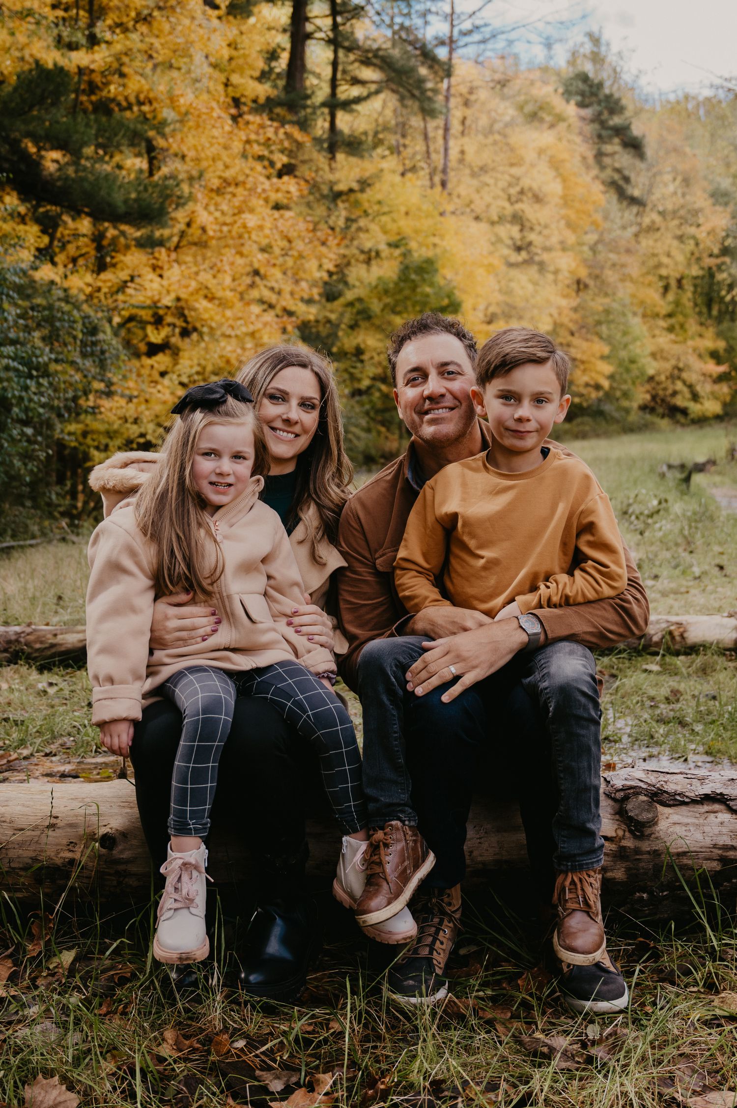 Happy family of four sitting on a log surrounded by vibrant autumn foliage in the forest.
